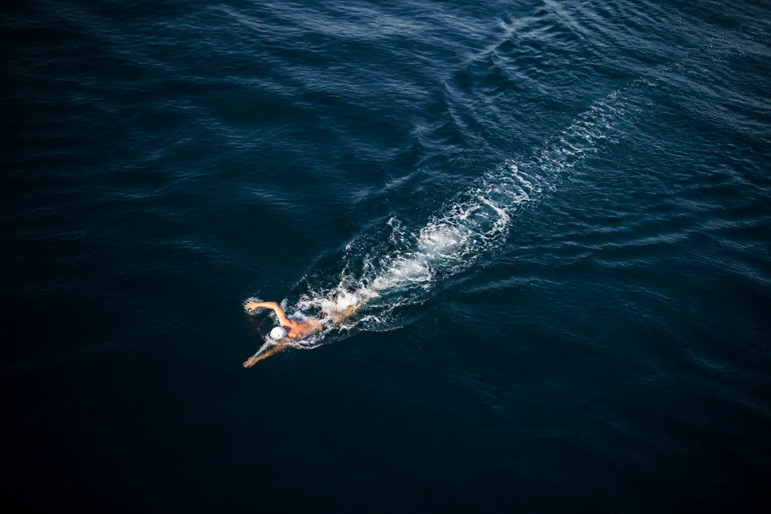 Open-water swimmer viewed from above, leaving a long wake in dark blue water